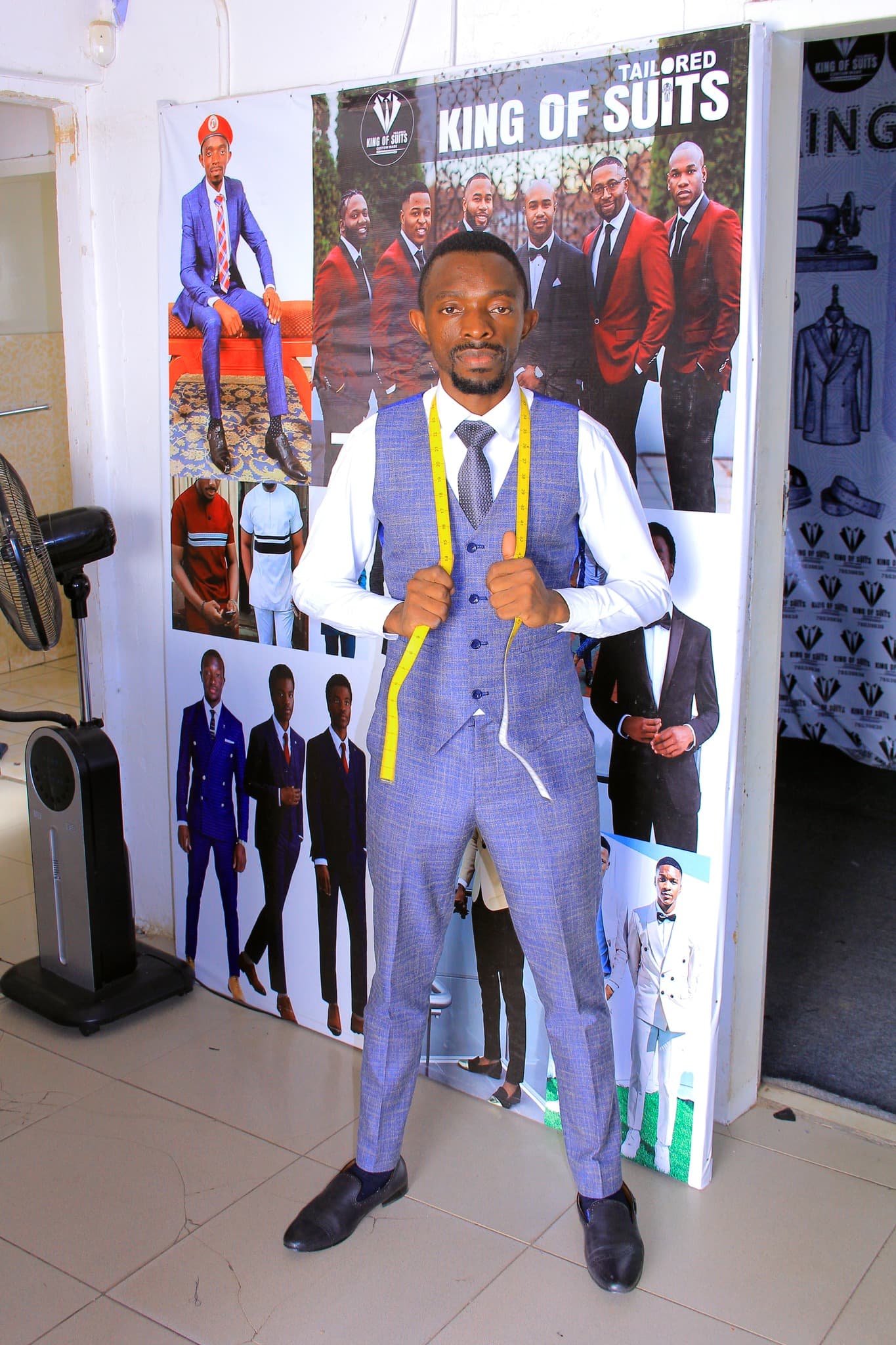 King of Suits tailor wearing a blue waistcoat and holding a measuring tape